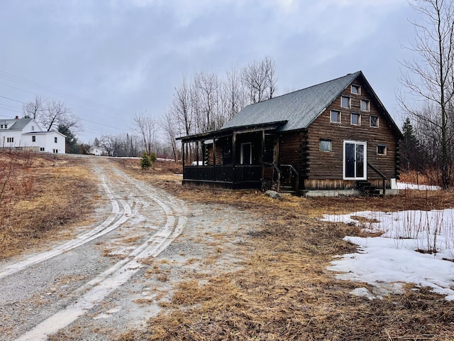 view of side of home featuring roof with shingles, a porch, log exterior, and dirt driveway