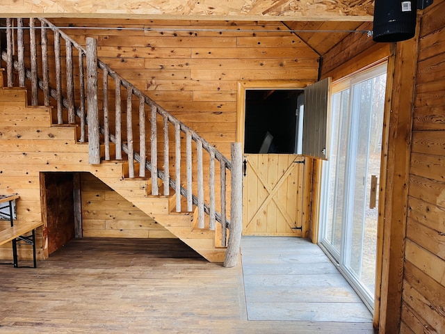 staircase featuring lofted ceiling, wood finished floors, wood walls, and a wealth of natural light