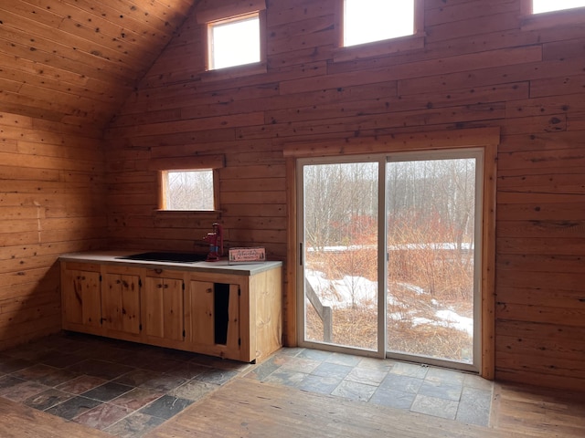 kitchen featuring wooden walls, high vaulted ceiling, stone tile flooring, a sink, and light countertops