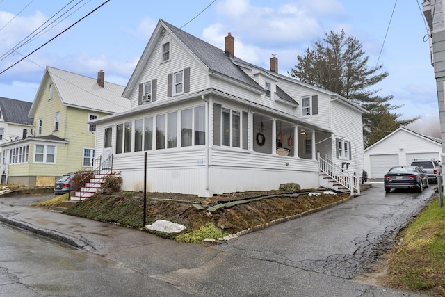 view of front of home featuring an outdoor structure, a sunroom, a garage, and a chimney