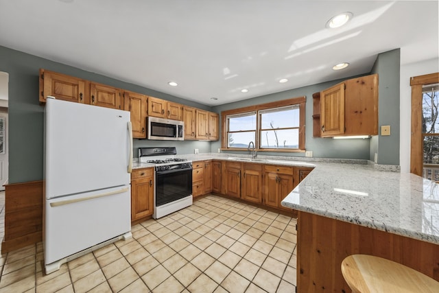 kitchen featuring light stone counters, recessed lighting, white appliances, a healthy amount of sunlight, and a sink