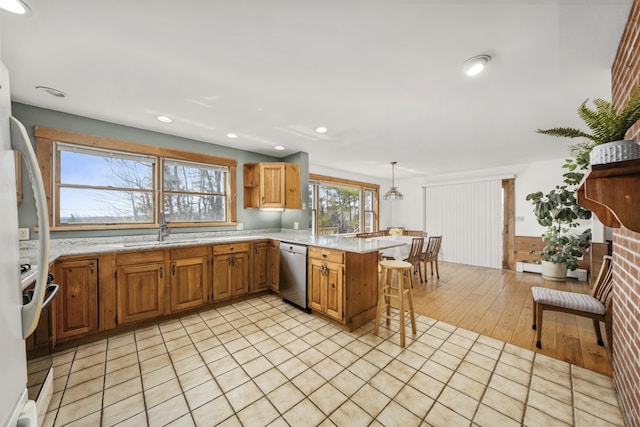 kitchen featuring a sink, freestanding refrigerator, a peninsula, stainless steel dishwasher, and a breakfast bar area