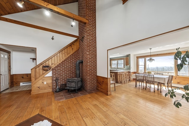 living room featuring high vaulted ceiling, beamed ceiling, a wood stove, a baseboard heating unit, and light wood finished floors