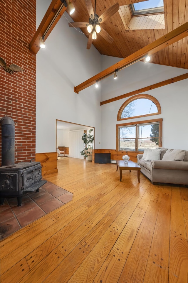 living room featuring a wood stove, a ceiling fan, beamed ceiling, wood-type flooring, and high vaulted ceiling