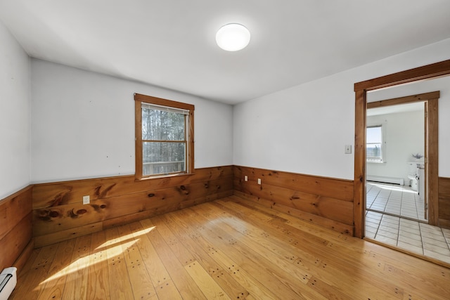 unfurnished room featuring wood walls, a baseboard heating unit, wainscoting, and plenty of natural light