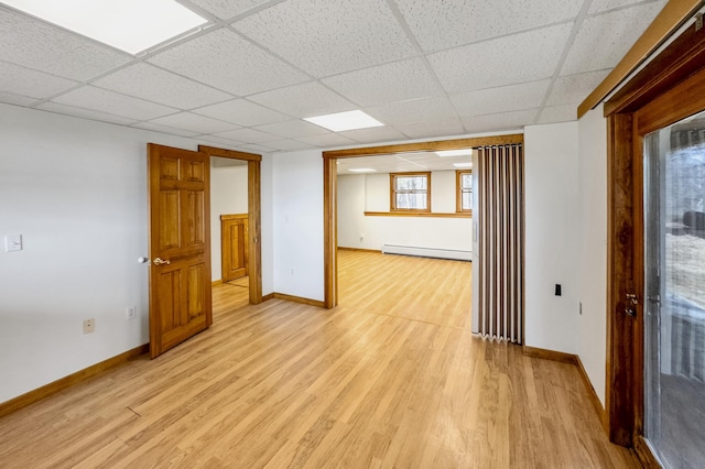 basement with light wood-style flooring, a paneled ceiling, and baseboard heating