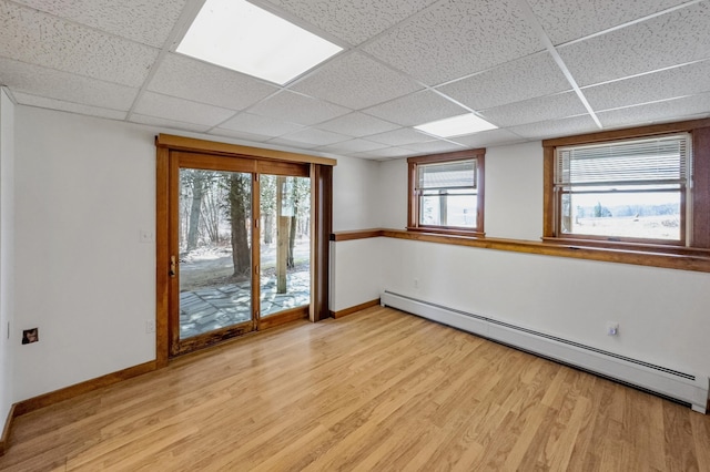 empty room featuring light wood-style flooring, a baseboard radiator, a paneled ceiling, and baseboards