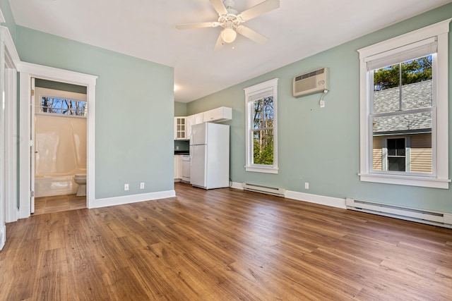 1 Old County Rd Unit 140, Wells, ME 04090 - unfurnished bedroom featuring freestanding refrigerator, a baseboard radiator, a wall unit AC, and multiple windows