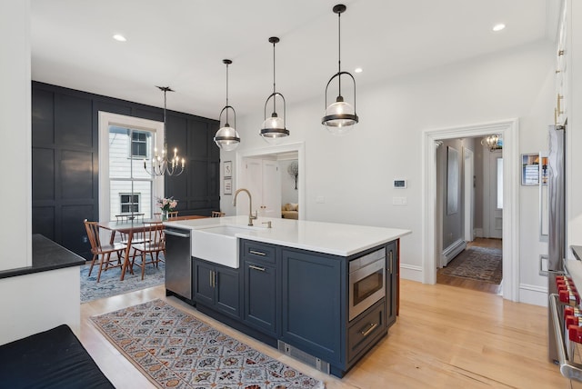 kitchen with a chandelier, a sink, light wood finished floors, appliances with stainless steel finishes, and hanging light fixtures