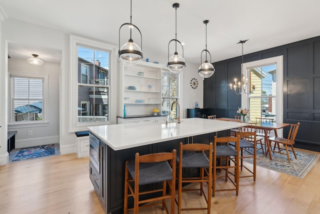 kitchen featuring light wood-style floors, pendant lighting, open shelves, and a center island with sink