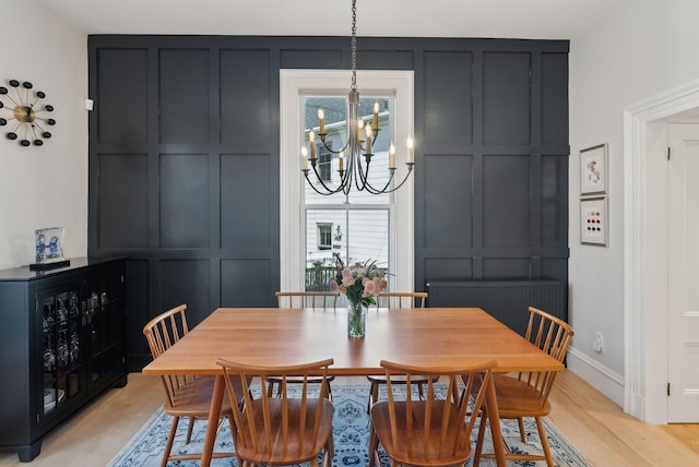 dining room with a chandelier, light wood-style flooring, and a decorative wall