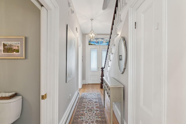 corridor with light wood-style floors, a notable chandelier, and baseboard heating