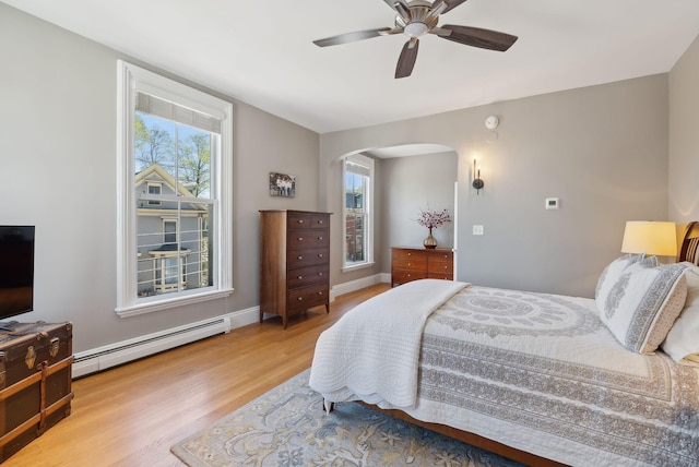 bedroom featuring arched walkways, a ceiling fan, baseboards, wood finished floors, and a baseboard radiator