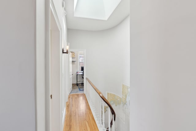 corridor featuring light wood-type flooring, a skylight, and an upstairs landing