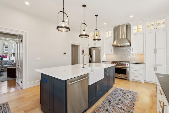 kitchen featuring white cabinets, a sink, light wood-style floors, wall chimney exhaust hood, and premium appliances