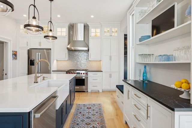 kitchen with decorative backsplash, high quality appliances, wall chimney exhaust hood, blue cabinets, and light wood finished floors