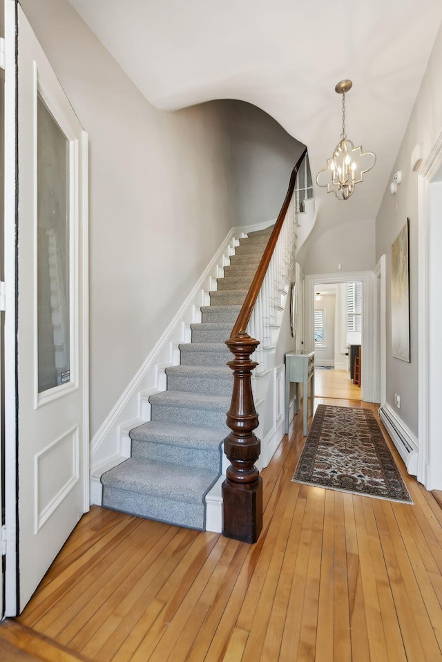 entryway with an inviting chandelier, baseboard heating, wood-type flooring, stairs, and lofted ceiling