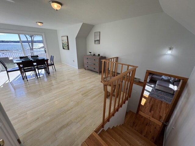stairs featuring vaulted ceiling, wood finished floors, and a water view