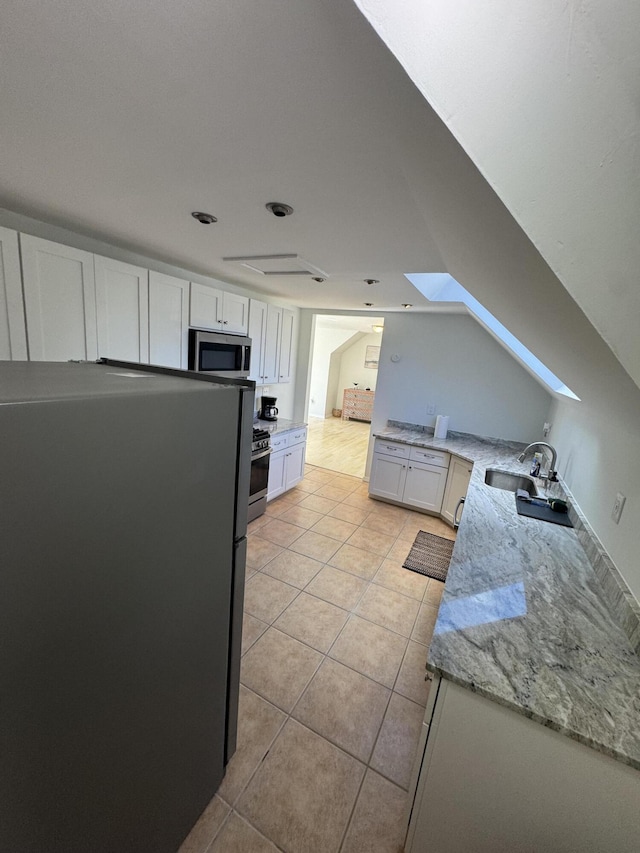 kitchen with white cabinets, stainless steel appliances, a sink, light stone countertops, and light tile patterned floors