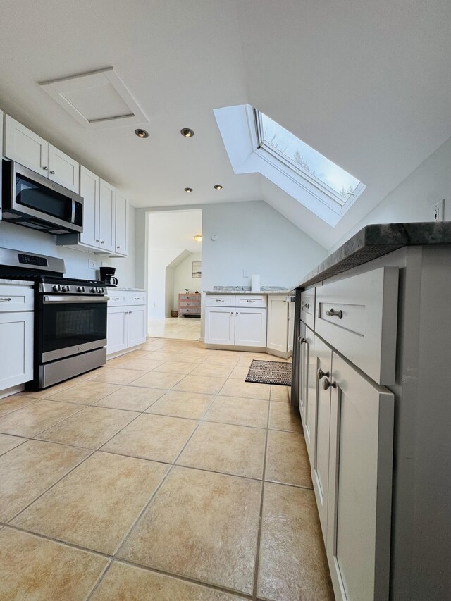 kitchen featuring white cabinets, stainless steel appliances, recessed lighting, vaulted ceiling with skylight, and light tile patterned floors