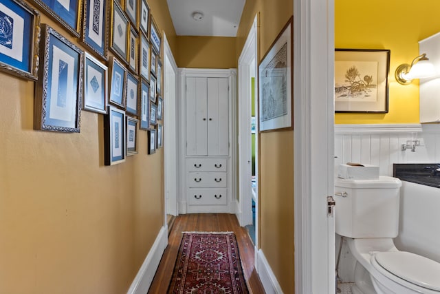 corridor with a wainscoted wall and wood finished floors
