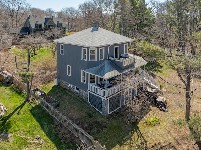 back of property with roof with shingles, fence, a chimney, a balcony, and a lawn