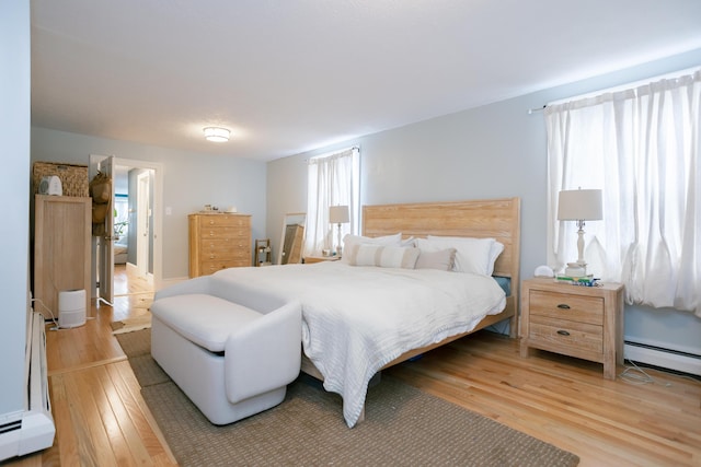 bedroom with a baseboard heating unit and light wood finished floors