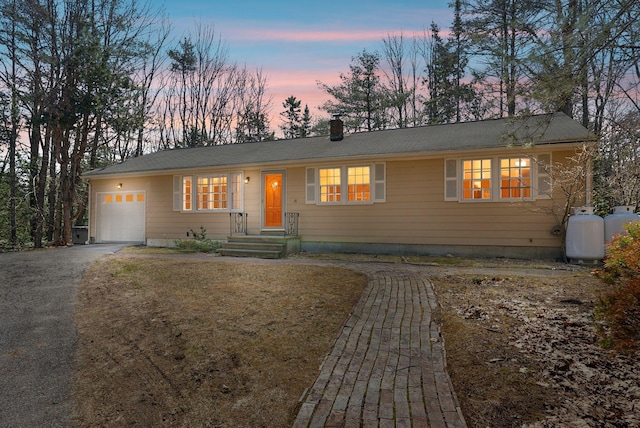 ranch-style home featuring a garage, a chimney, and aphalt driveway