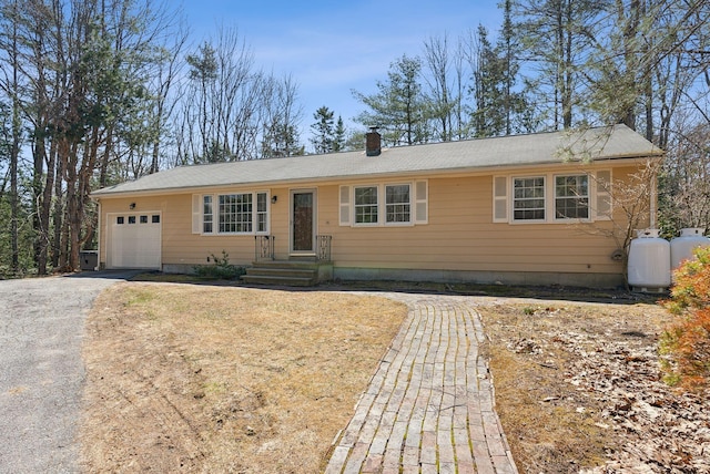 ranch-style home featuring an attached garage, driveway, and a chimney
