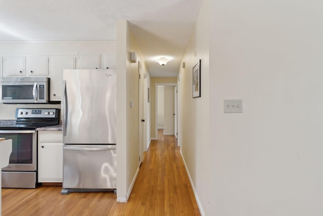 kitchen featuring light wood-style flooring, baseboards, white cabinetry, and appliances with stainless steel finishes