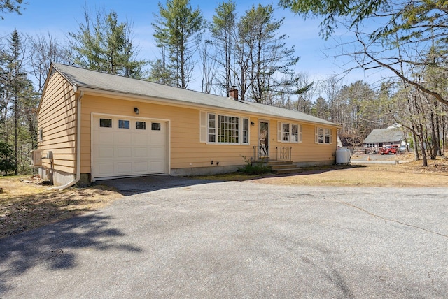 ranch-style house with a chimney, aphalt driveway, and a garage
