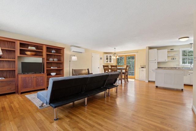 living room featuring light wood-style flooring, a textured ceiling, and a wall mounted air conditioner
