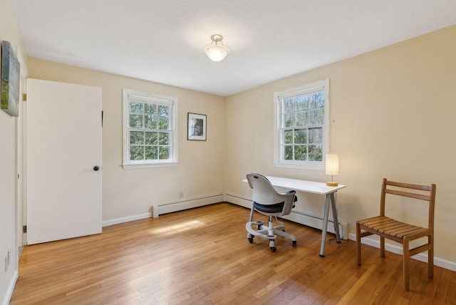 home office with a baseboard heating unit, plenty of natural light, and light wood-style flooring