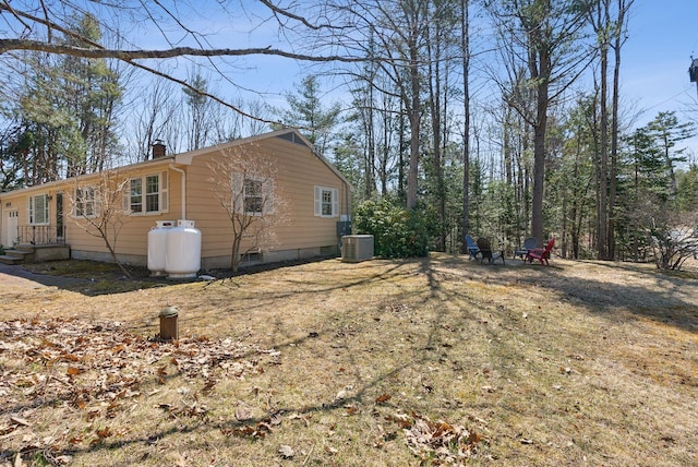 view of side of property with an outdoor fire pit, a chimney, and central air condition unit