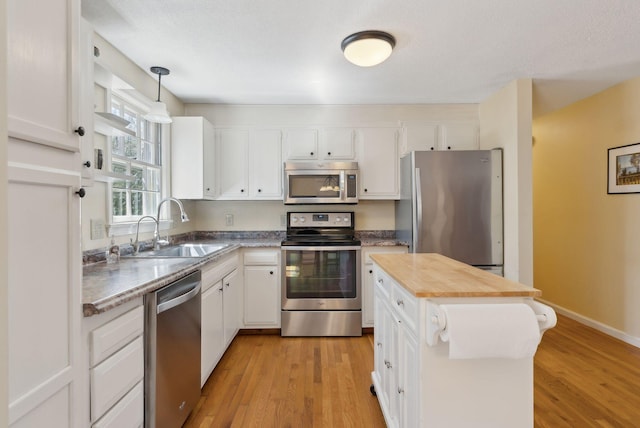 kitchen featuring light wood finished floors, a sink, pendant lighting, appliances with stainless steel finishes, and white cabinetry