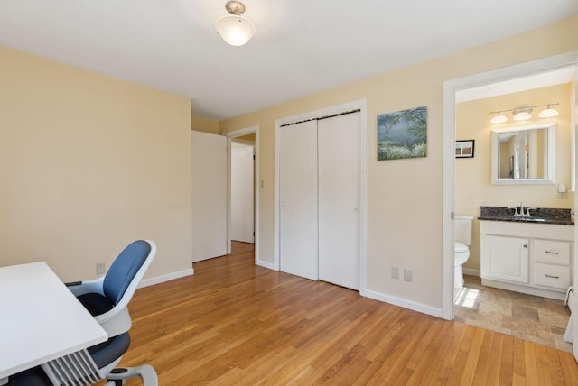 home office featuring light wood finished floors, baseboards, and a sink