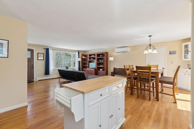 kitchen featuring baseboard heating, a wall mounted AC, light wood-type flooring, pendant lighting, and white cabinetry
