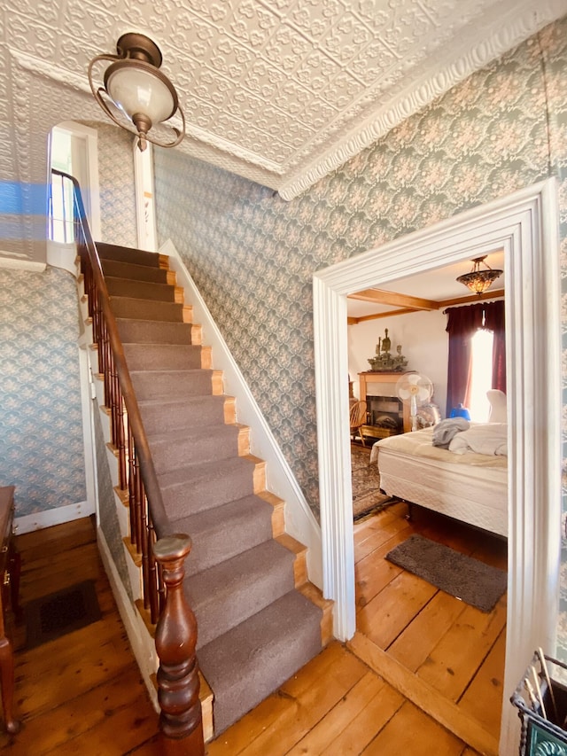 stairway featuring an ornate ceiling, wood-type flooring, visible vents, baseboards, and wallpapered walls