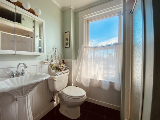 half bathroom featuring crown molding, baseboards, toilet, tile patterned flooring, and wainscoting