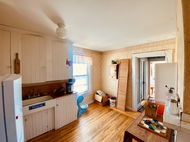 kitchen with wallpapered walls, a sink, baseboards, and light wood-style floors