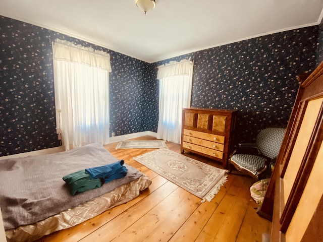 bedroom featuring baseboards, wallpapered walls, ornamental molding, and hardwood / wood-style flooring