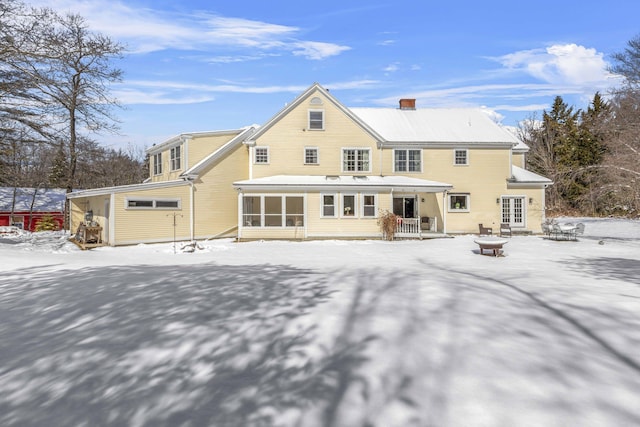 snow covered house featuring a chimney, a sunroom, and an outdoor fire pit