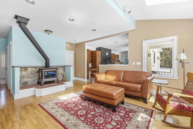 living room featuring a skylight, baseboards, a wood stove, and light wood-type flooring
