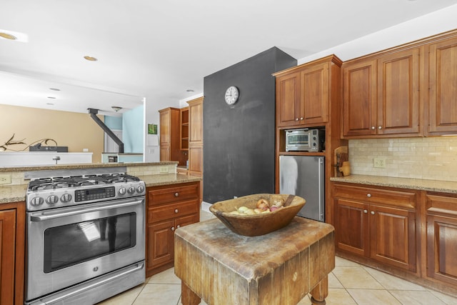 kitchen with brown cabinetry, backsplash, light stone counters, stainless steel appliances, and light tile patterned flooring