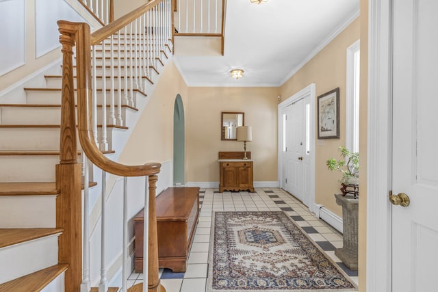 foyer featuring crown molding, baseboard heating, arched walkways, baseboards, and stairway