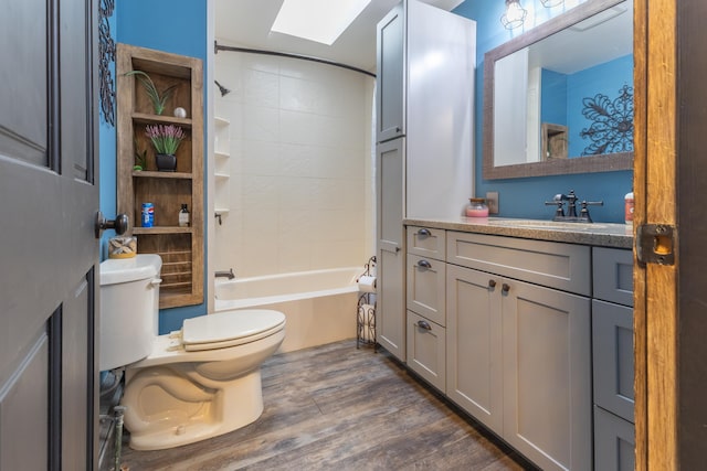 full bath featuring toilet, vanity, wood finished floors, a skylight, and washtub / shower combination