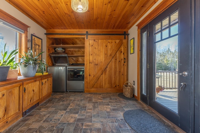 clothes washing area with wooden ceiling, a barn door, washing machine and dryer, stone finish flooring, and laundry area