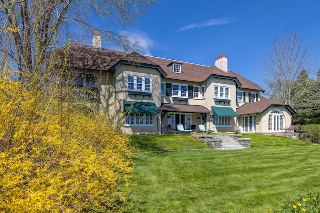 rear view of property featuring a chimney, french doors, a yard, and stucco siding