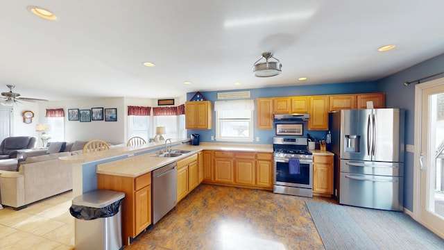 kitchen featuring light countertops, stainless steel appliances, under cabinet range hood, a sink, and open floor plan