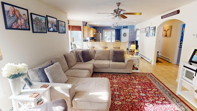 living area featuring arched walkways, light tile patterned floors, ceiling fan, and baseboard heating